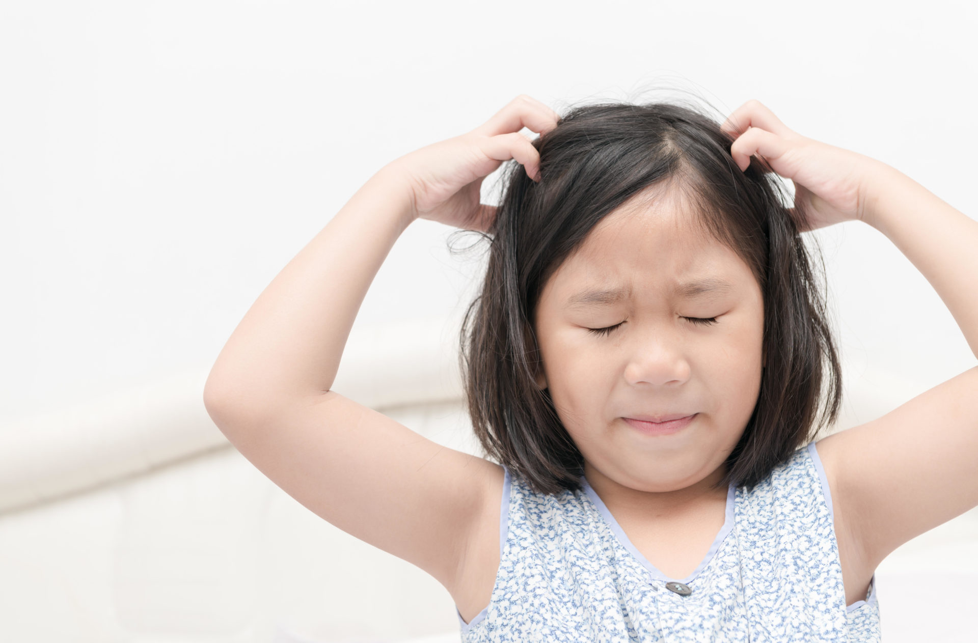 Child scratching her hair for head lice. Image: Mother checking childrens head for lice with a comb. 