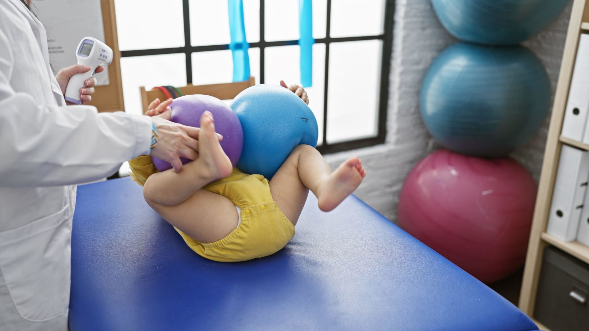 A paediatrician checks a baby's flexibility with colourful balls at a physiotherapy centre
