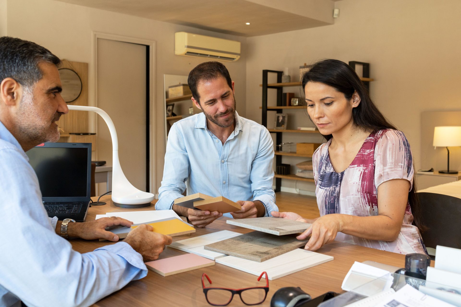 Serious clients with material samples of facades of kitchen cabinets and discussing details with interior designer in office of furniture store.