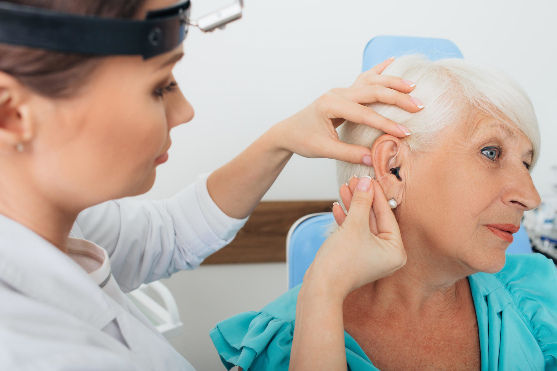 Doctor helping elderly woman inserting hearing aid. 